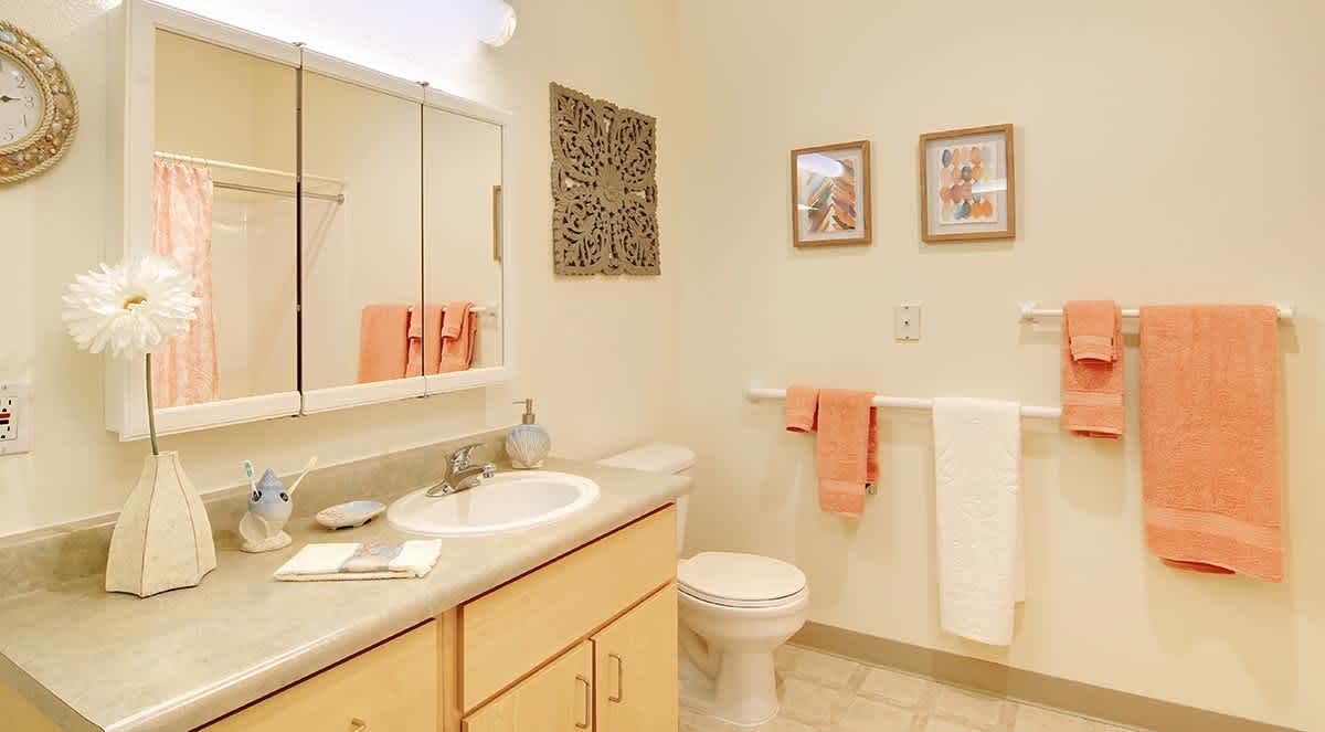 A neatly organized bathroom featuring a sink with a mirrored cabinet, toilet, and towels hanging on the wall.