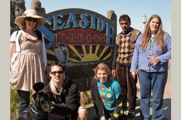 A group of friends posing in front of a 'Seaside' sign on a sunny day.