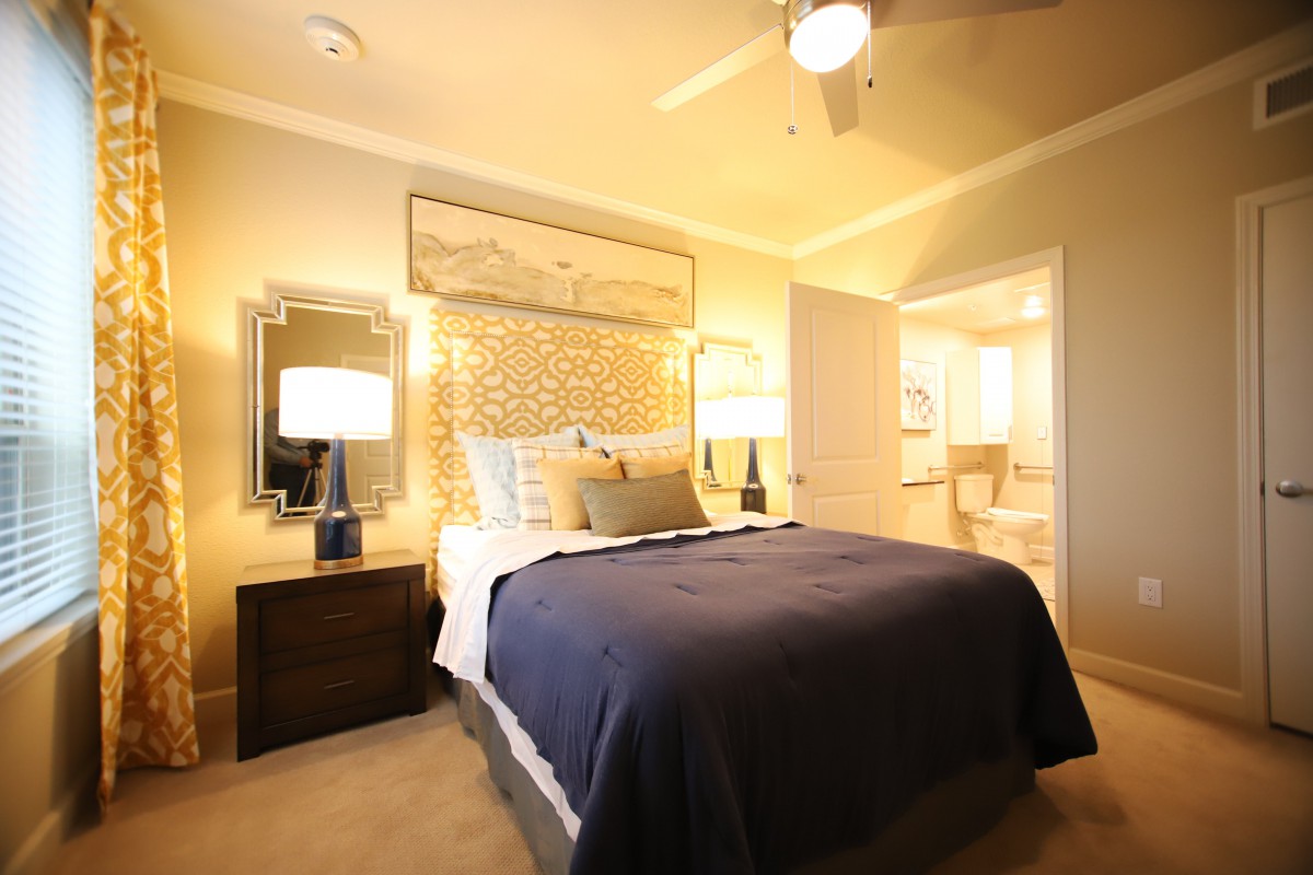 A cozy bedroom with a neatly made bed, flanked by nightstands and lamps, featuring warm lighting and elegant decor.