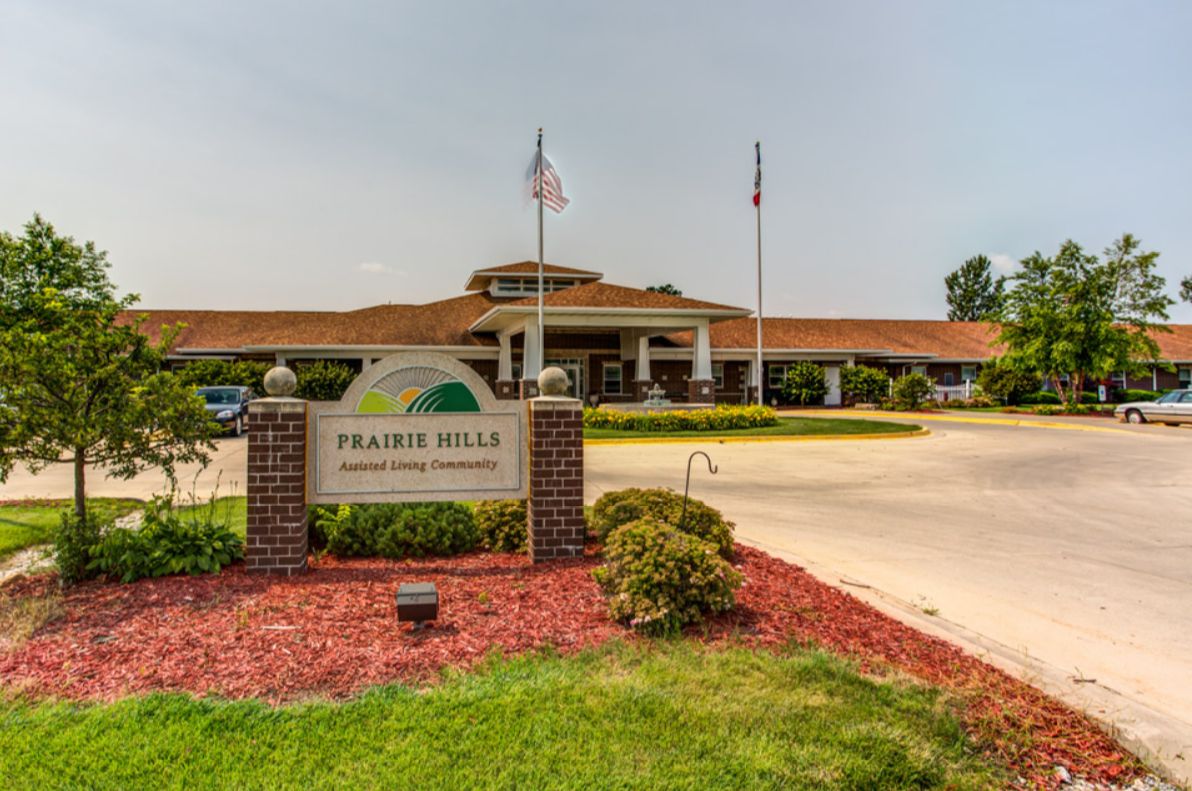 Entrance to a building with a sign labeled 'Prairie Hills Assisted Living Center' and landscaped surroundings.