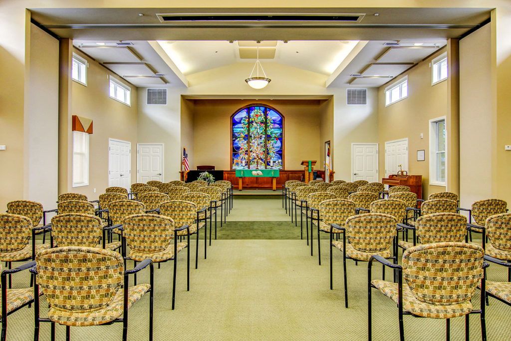 A peaceful chapel interior with rows of chairs and a stained glass window at the front.