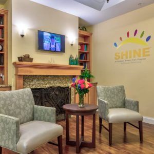 A cozy waiting area with comfortable chairs, a television, and a fireplace adorned with floral decor.