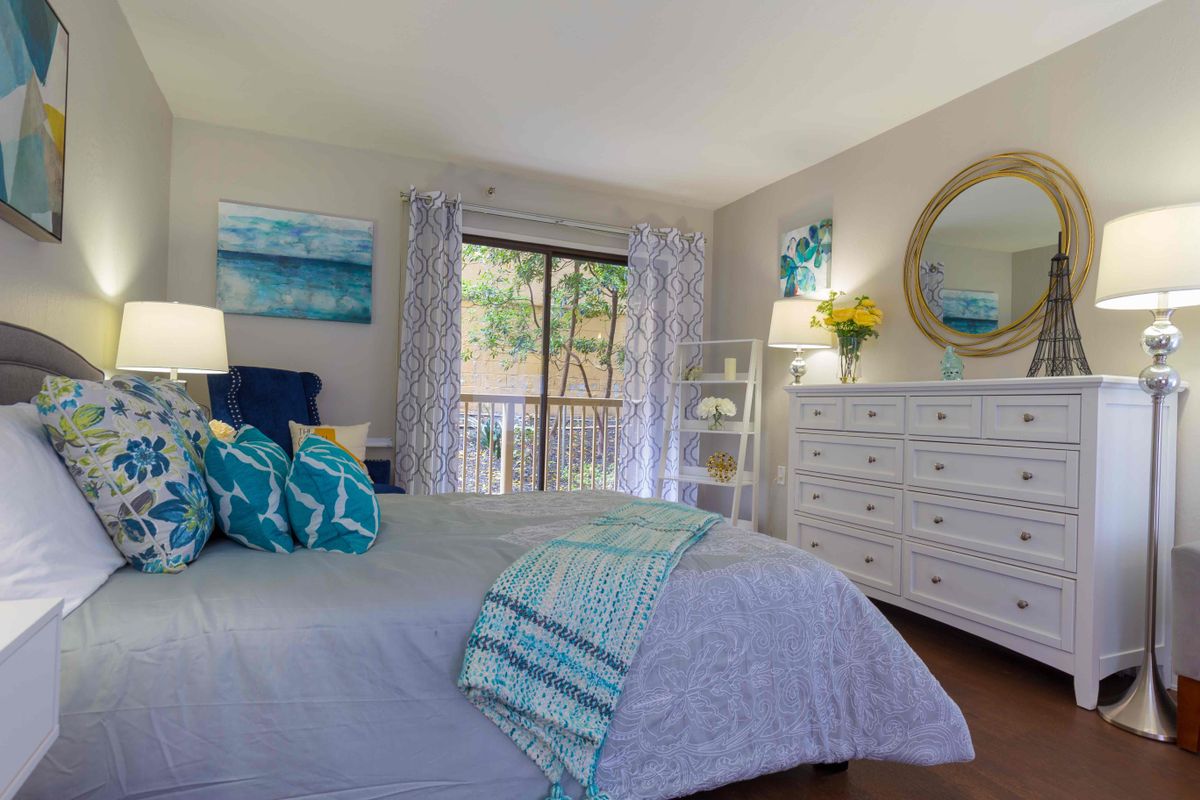 A cozy bedroom with elegant decor, featuring a large bed, white furniture, and natural light streaming through a window.