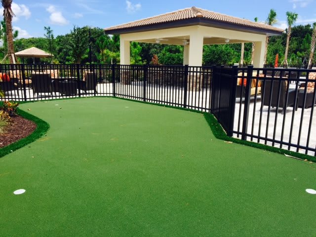 An outdoor dog park with artificial turf and a shaded seating area.