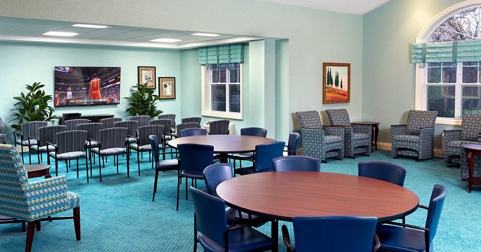 A well-lit seating area with round tables and blue chairs, featuring artwork on the walls and a large window.