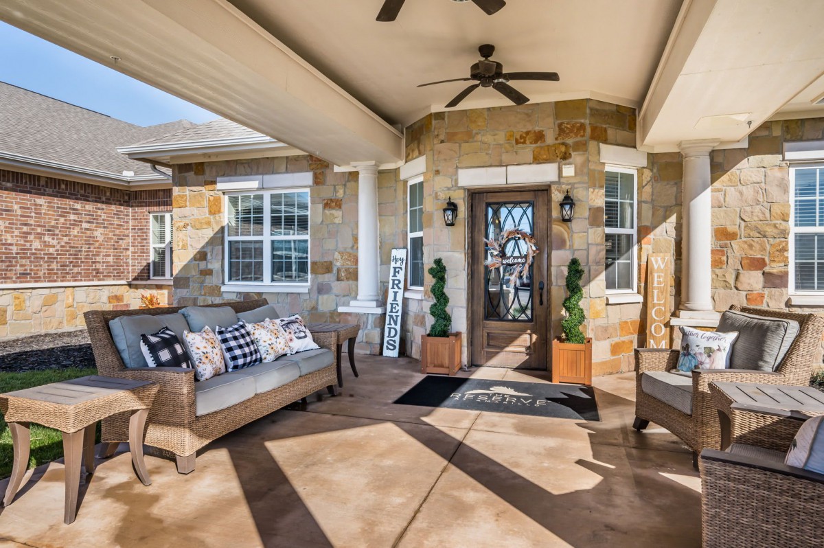 A cozy patio with comfortable outdoor seating, ceiling fan, and stone facade accentuates the relaxing ambiance.