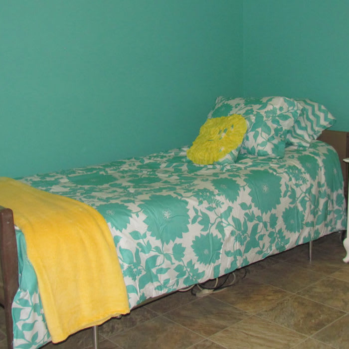 A bedroom with a single bed featuring teal and white bedding, accented by a yellow blanket and pillow.