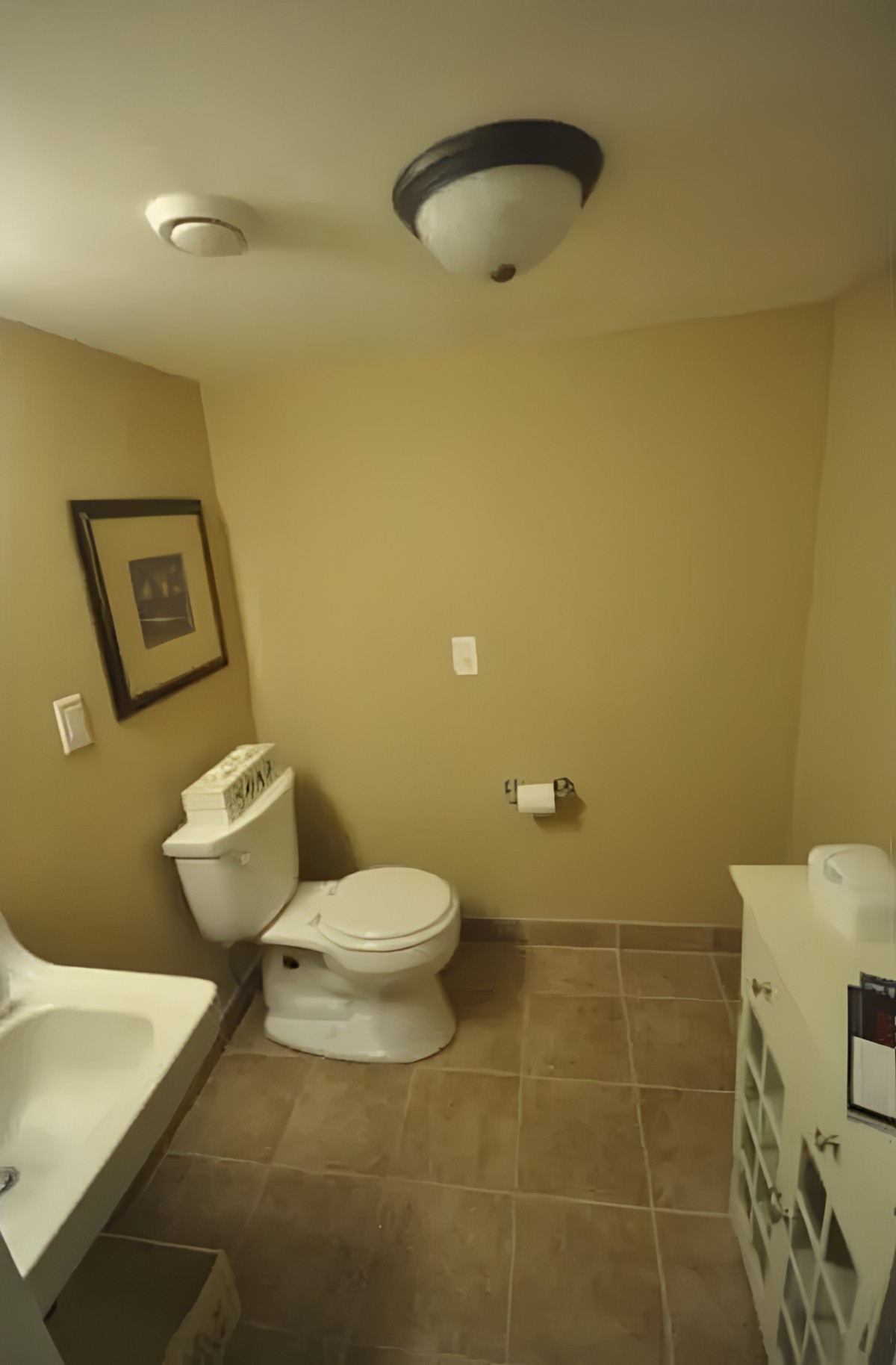 A minimalist bathroom featuring a toilet and sink with beige walls and tile flooring.