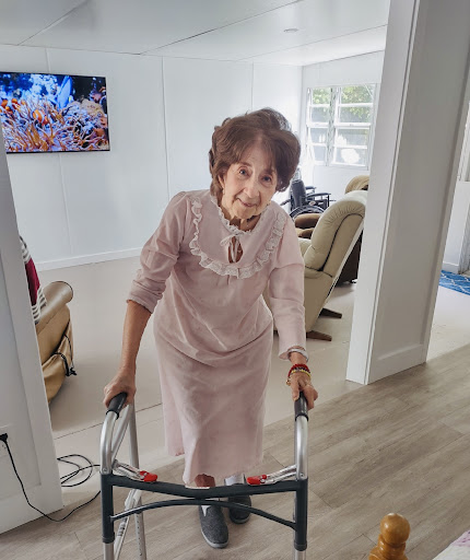 An elderly woman using a walker in a bright living room.