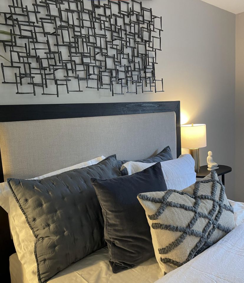 A modern bedroom with stylish decor, featuring a bed with multiple pillows and abstract wall art.