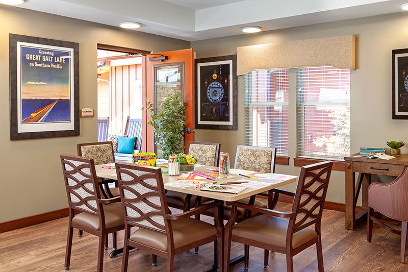 A well-decorated dining room featuring a large table surrounded by chairs, with artwork on the walls and plenty of natural light.