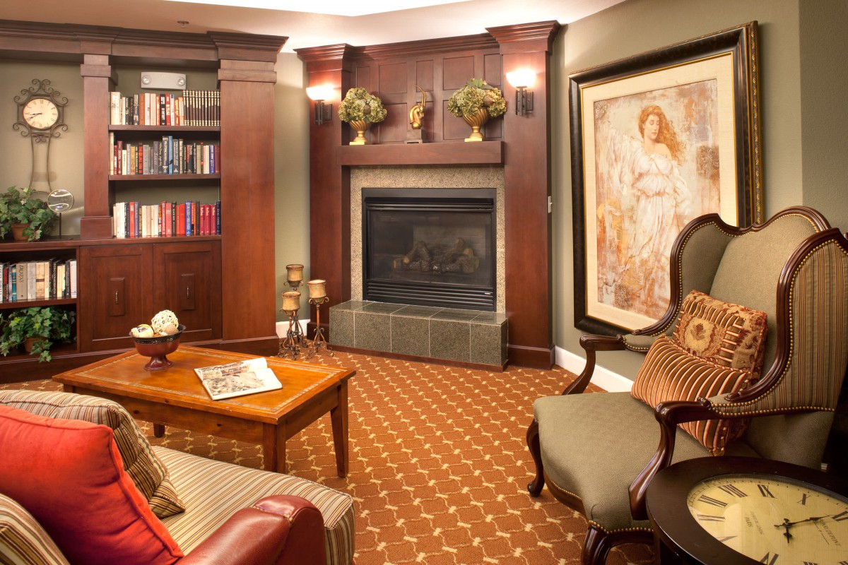 A cozy living room featuring a fireplace, armchairs, and a bookshelf filled with books.