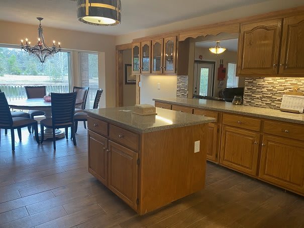 A spacious open kitchen with wooden cabinets and an island, adjacent to a dining area with a chandelier.