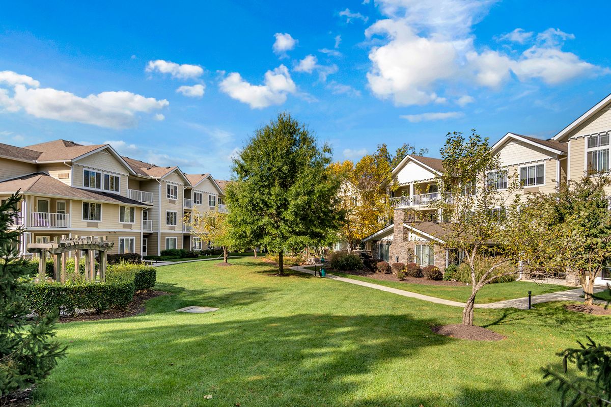 A scenic view of a residential apartment complex with well-maintained green spaces and trees under a clear blue sky.