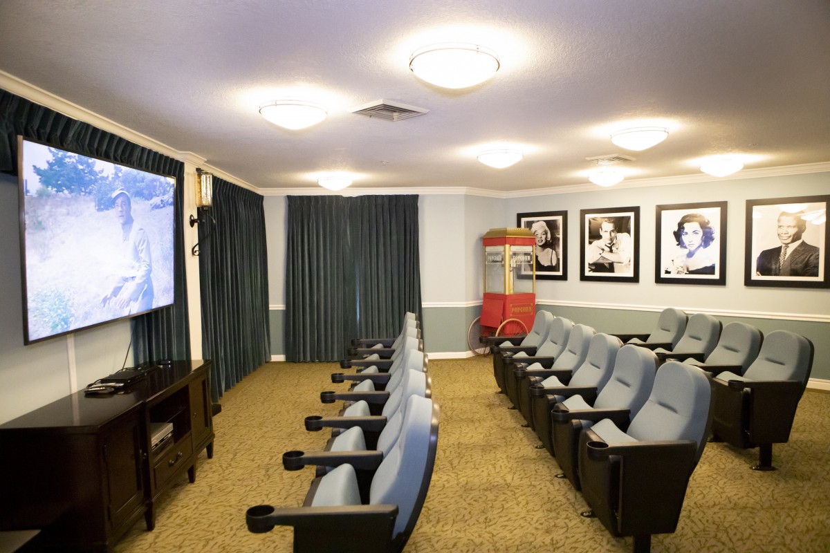 A cozy home theater setup with rows of comfortable seating, a large projector screen, and vintage-style movie decor.