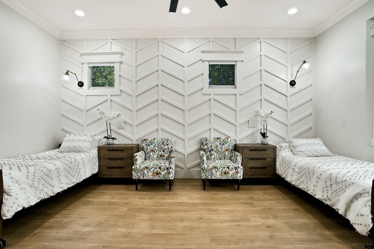 A modern bedroom with twin beds, nightstands, and armchairs, featuring wood flooring and stylish wall decor.