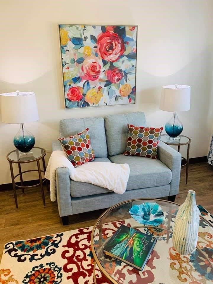 A cozy living room with a light blue sofa, vibrant floral painting, and colorful decorative accents.