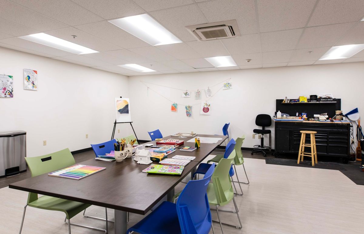 A bright and organized classroom or art studio with tables, chairs, and art supplies neatly arranged.