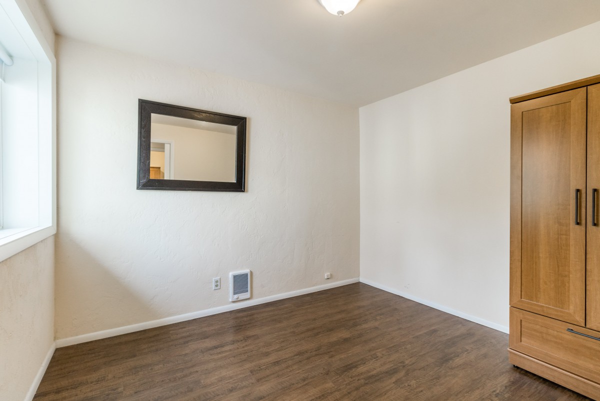 A minimalist empty room featuring hardwood floors and a wall-mounted mirror.
