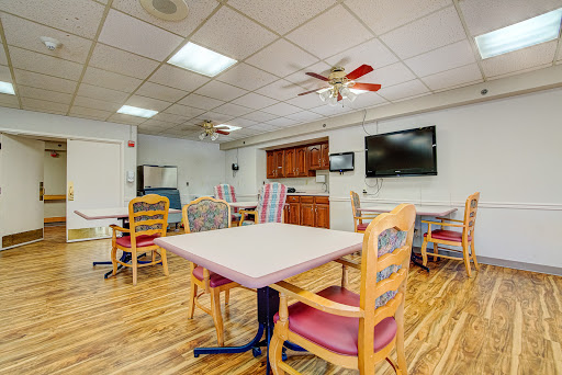 A spacious dining area featuring several tables and chairs, with a kitchenette and a television on the wall.