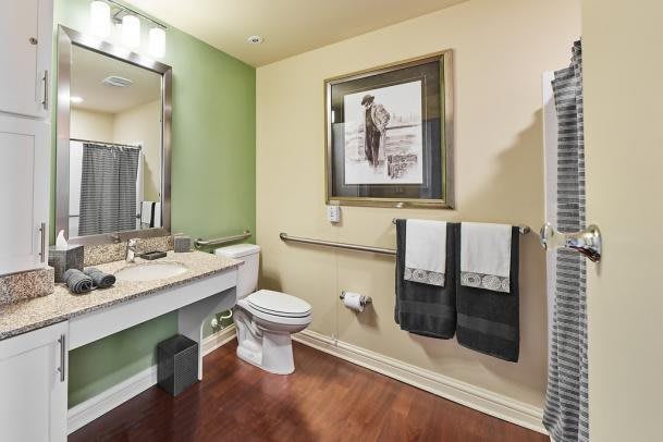 A well-decorated bathroom with a toilet, sink, and mirror, featuring modern artwork and accessible design elements.