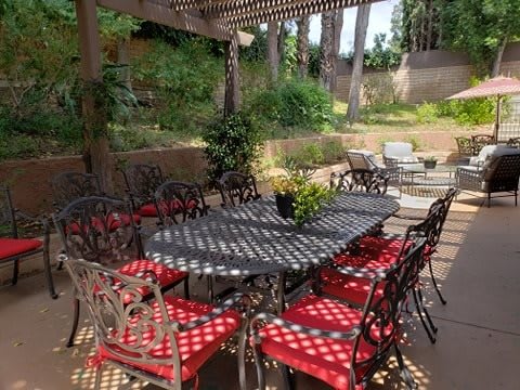 A beautifully arranged outdoor patio with a large table and red-cushioned chairs under a pergola.