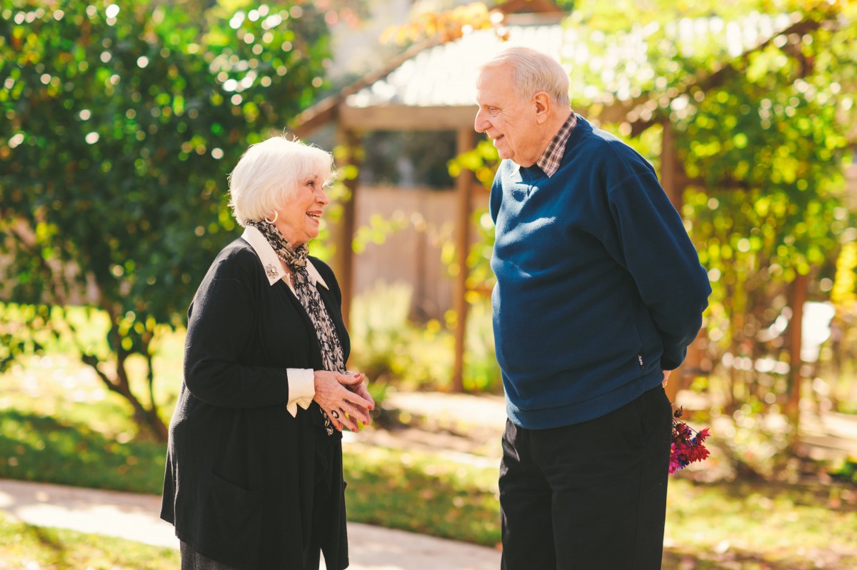An elderly couple enjoying a conversation in a sunny garden.