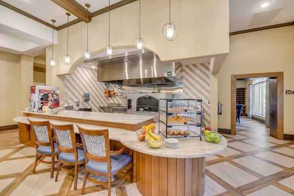 A modern kitchen interior with a central counter and bar stools, featuring hanging lights and cooking equipment.