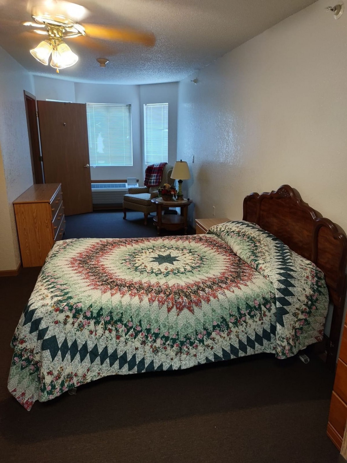 A cozy bedroom with a colorful quilt on the bed and natural light coming in through the windows.