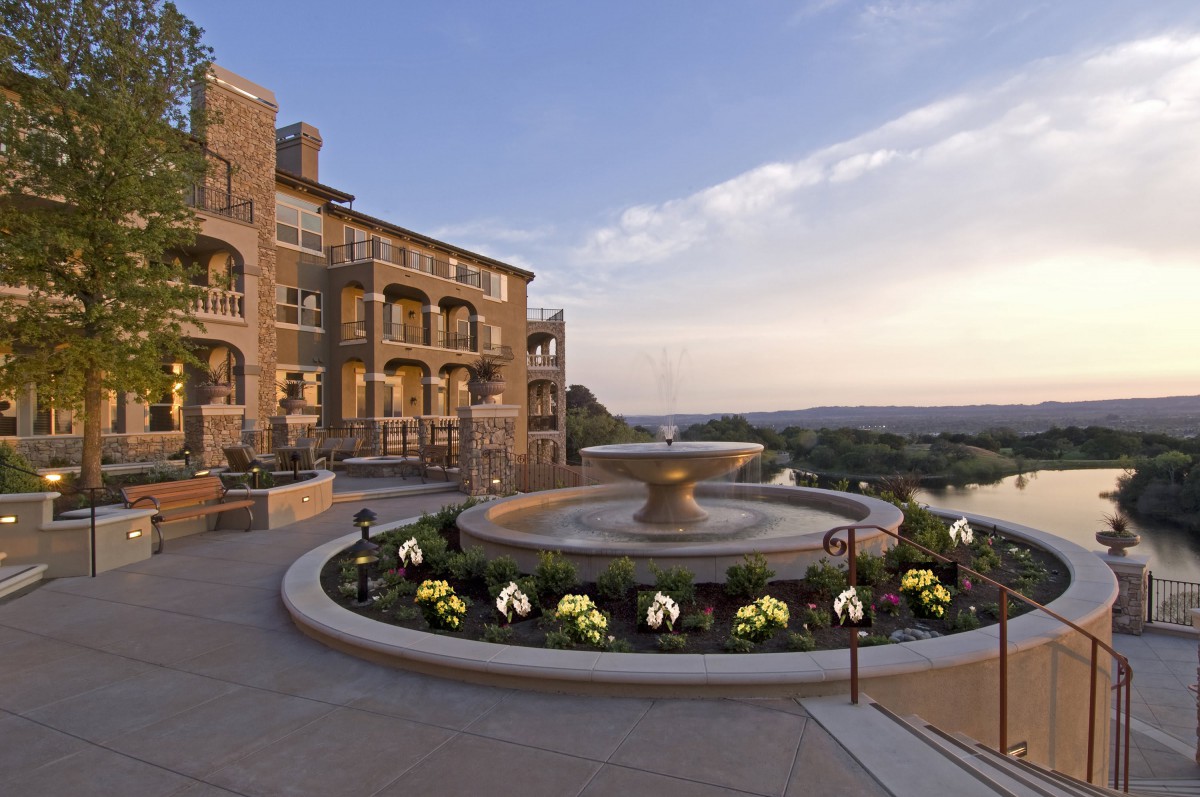 A luxurious hotel building with elegant balconies and a central fountain, set against a stunning sunset backdrop.