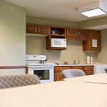 A kitchen area with wooden cabinets, a microwave, stove, and chairs around a table.