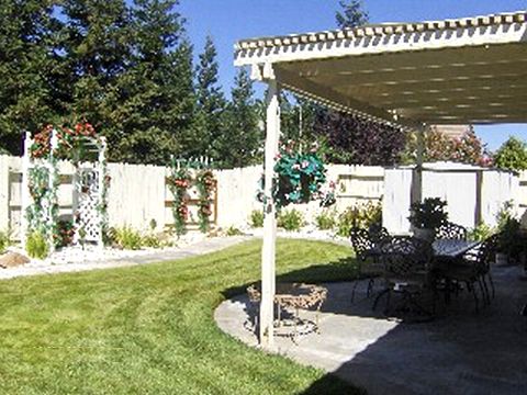 A sunny backyard with a patio and pergola, featuring a well-maintained lawn and garden.