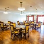 A spacious dining room with multiple tables and chairs, featuring elegant lighting and hardwood flooring.