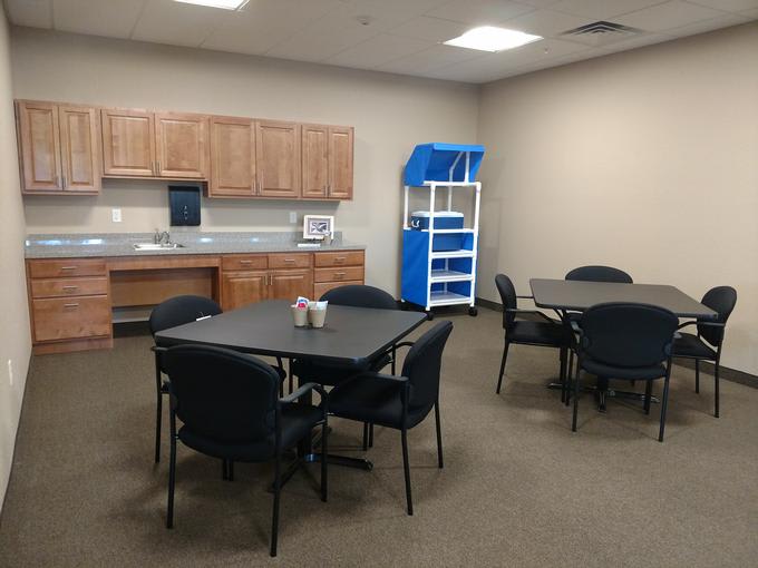 An office break room with tables, chairs, and a kitchenette.