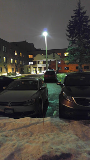 A quiet parking lot at night, illuminated by a streetlight, with parked cars and snow on the ground.