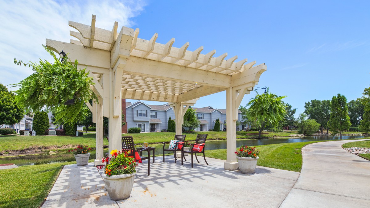 A welcoming outdoor patio with a wooden pergola, surrounded by a garden and vibrant flowers.