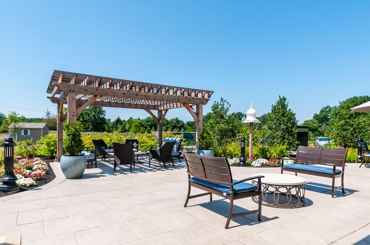 A spacious outdoor patio featuring a pergola, comfortable seating, and a fire pit surrounded by lush landscaping on a sunny day.