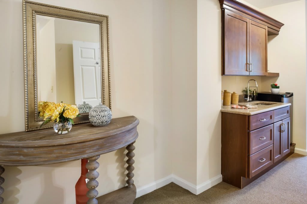 A cozy home interior featuring a wooden table with decorative items and a mirror, adjacent to a kitchen area.