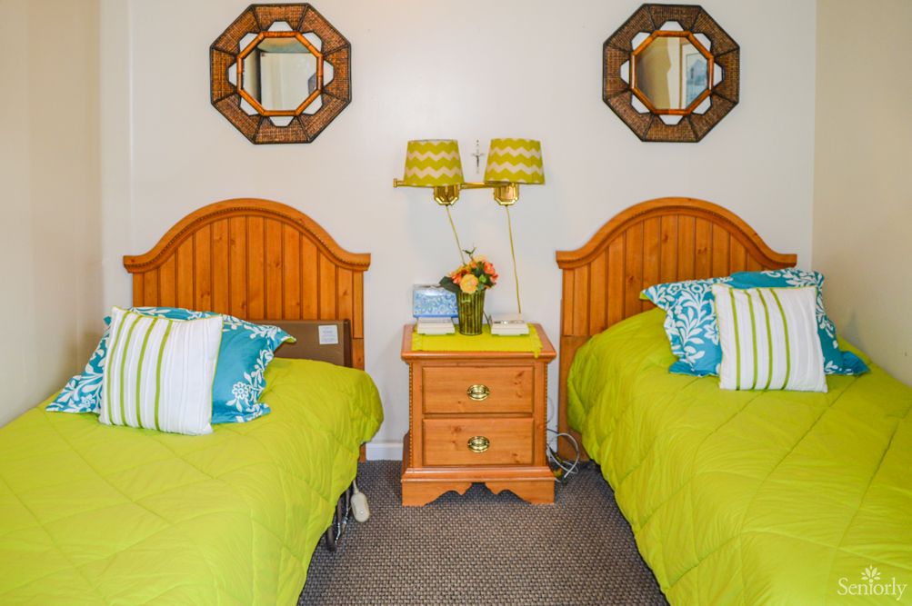 A cozy bedroom with two twin beds featuring wooden headboards, vibrant pillows, and a central nightstand adorned with decorative lamps and mirrors.