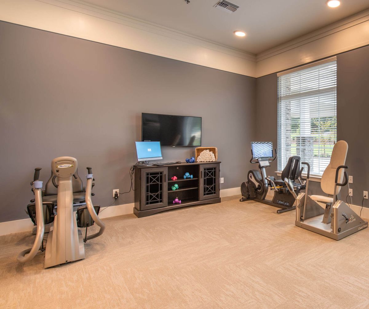 A home exercise room featuring fitness equipment and a television, with natural light streaming in through large windows.
