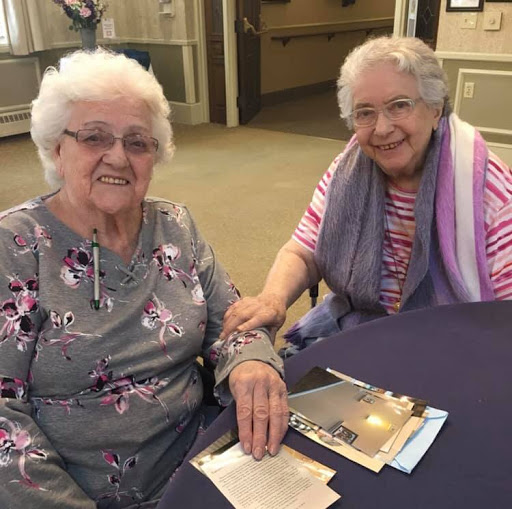 Two elderly women enjoying each other's company in a care facility.