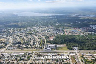 An aerial view of a suburban area with roads, buildings, and surrounding natural landscape.