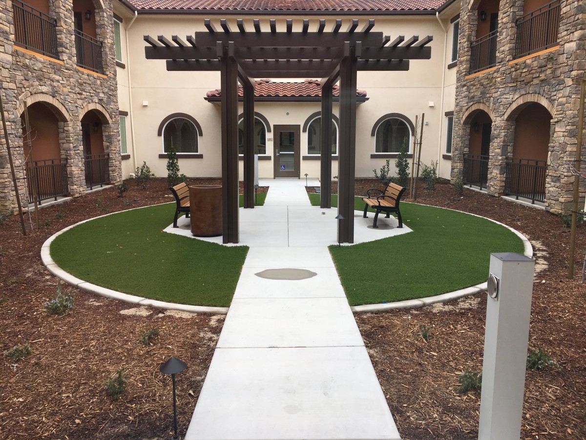 A beautifully landscaped courtyard featuring a central pergola and benches along a circular pathway.