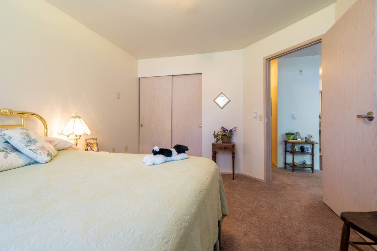 A cozy bedroom with a neatly made bed, lamp, and closet doors visible.