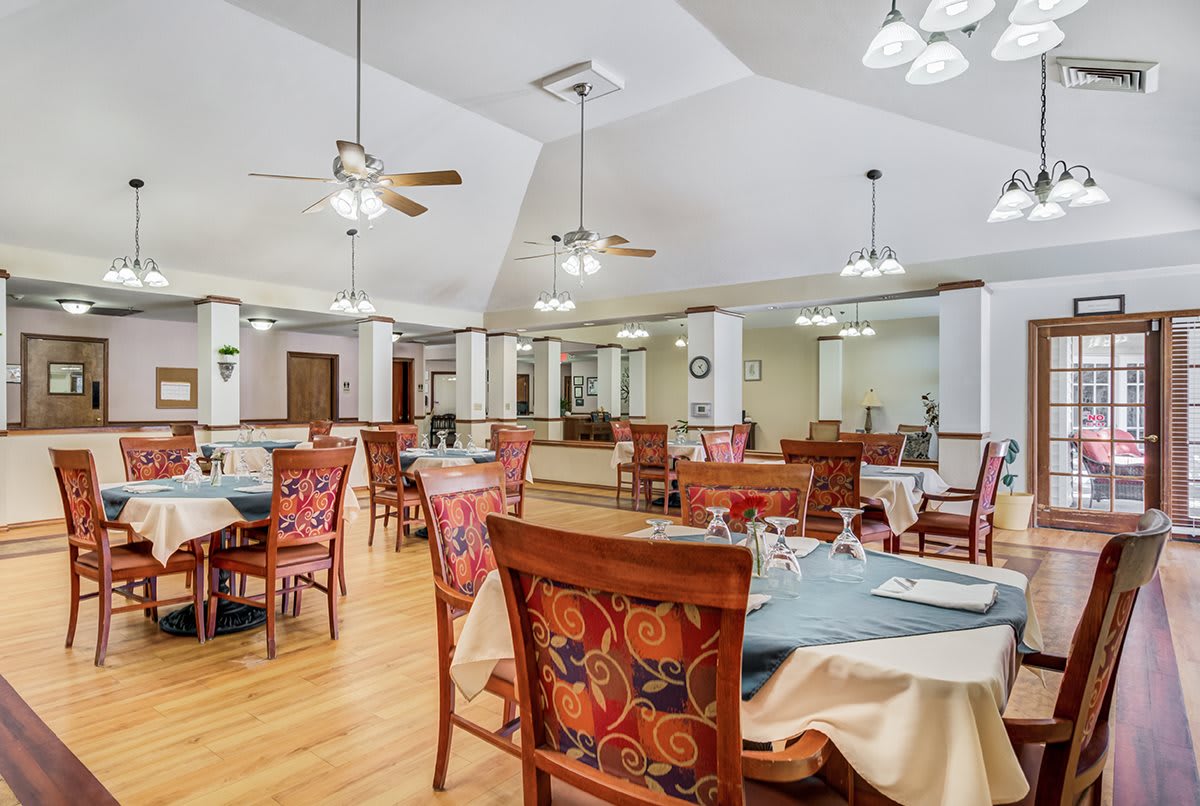 A spacious and elegantly decorated dining room featuring tables with colorful chairs, set with glassware under ceiling fans.
