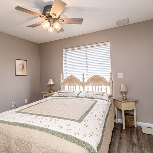 A cozy bedroom featuring a bed with a decorative quilt, flanked by nightstands and lamps, under a ceiling fan.