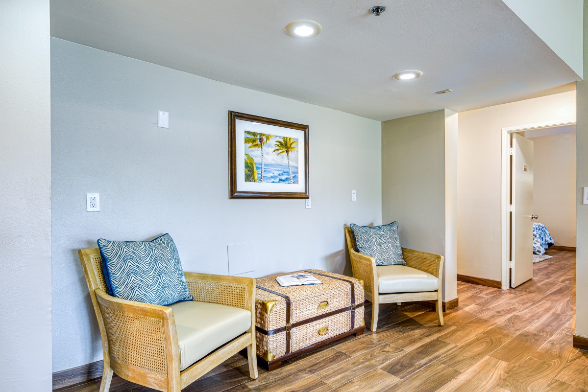 A cozy lounge area with two wicker chairs and a decorative chest, complemented by a framed beach scene on the wall.