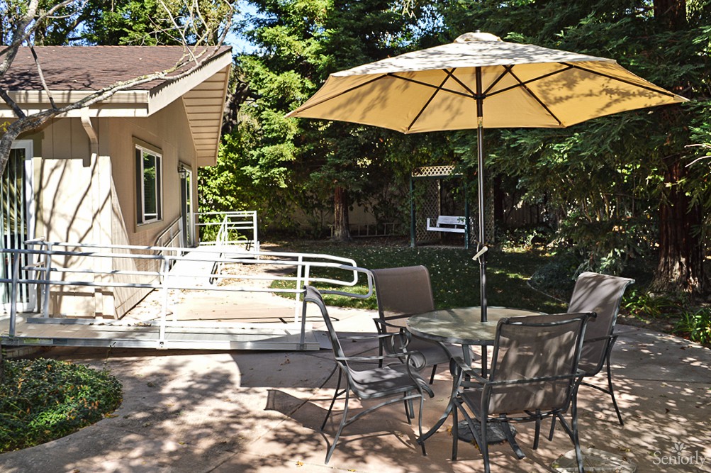 A sunny backyard patio with outdoor furniture, including a table, chairs, and an umbrella.