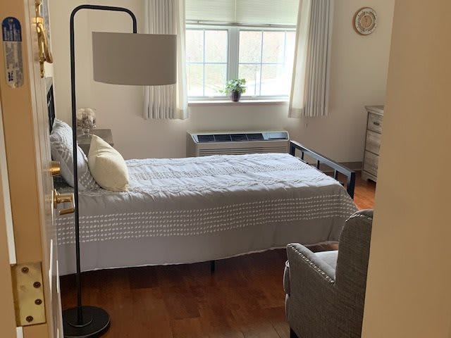 A minimalist bedroom with a single bed, a lamp, and an armchair next to a window.