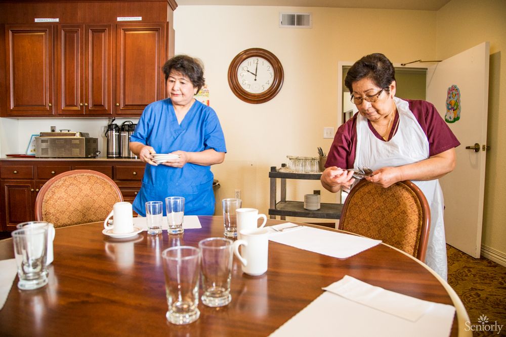 Two people cleaning a kitchen table, preparing glasses and cups.
